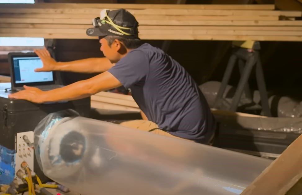 An Atlas Home Energy Solutions emplyee working on a computer behind an Aeroseal machine and tube