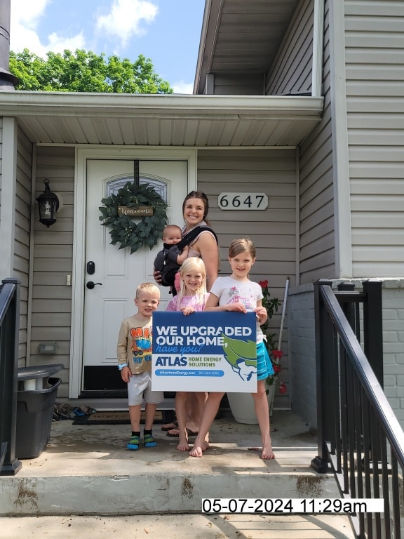 A family standing in front of their upgraded home and holding an Atlas yard sign